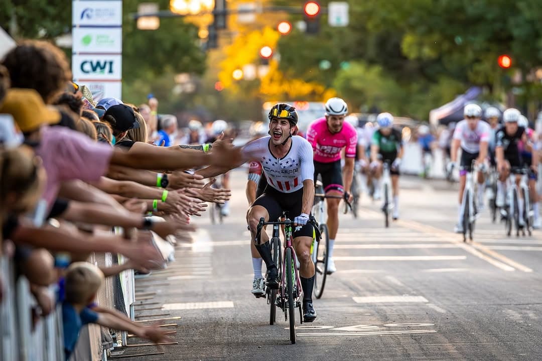 A national-level criterium rider celebrating beside a crowd at a downtown race